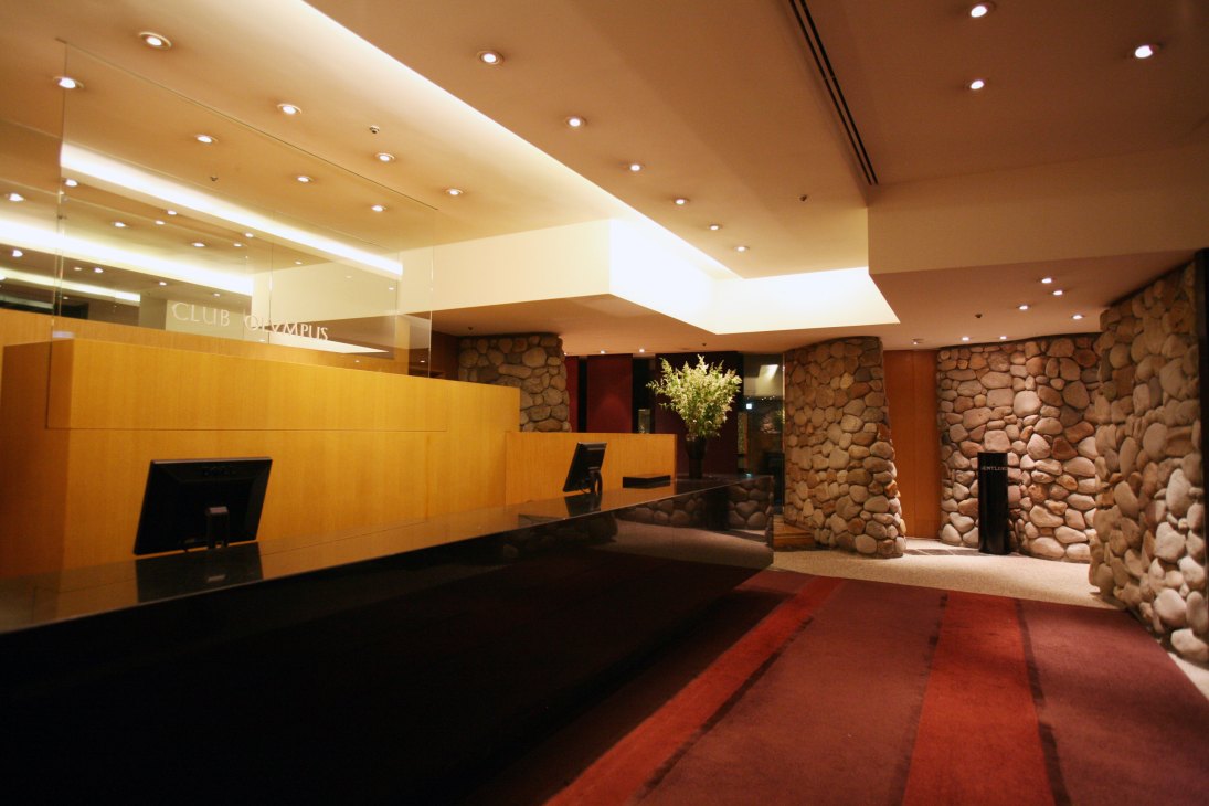 Modern hotel lobby with wooden reception desk, stone accent walls, and ambient ceiling lighting.