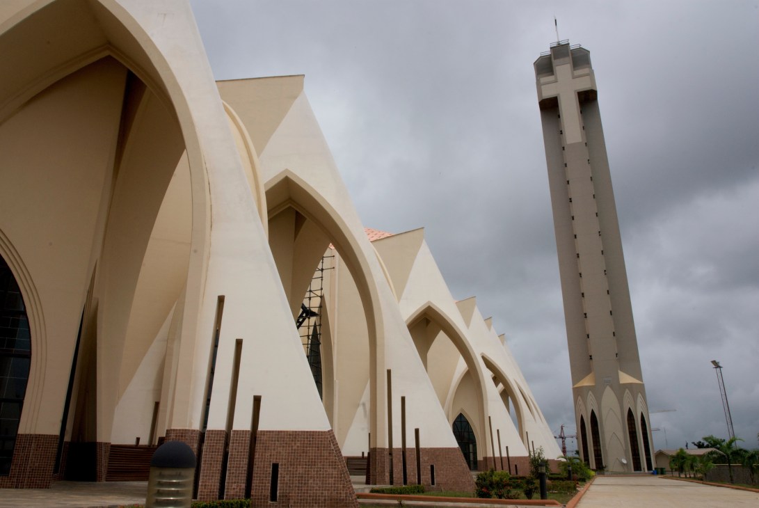 The Nigerian National Christian Centre with white arched architecture and tall minaret-style tower against cloudy sky.