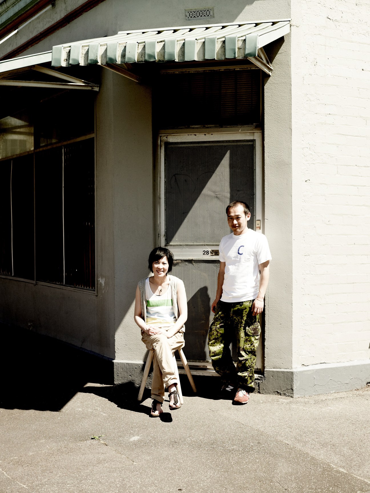 Two people standing outside a building entrance in bright sunlight casting dramatic shadows.