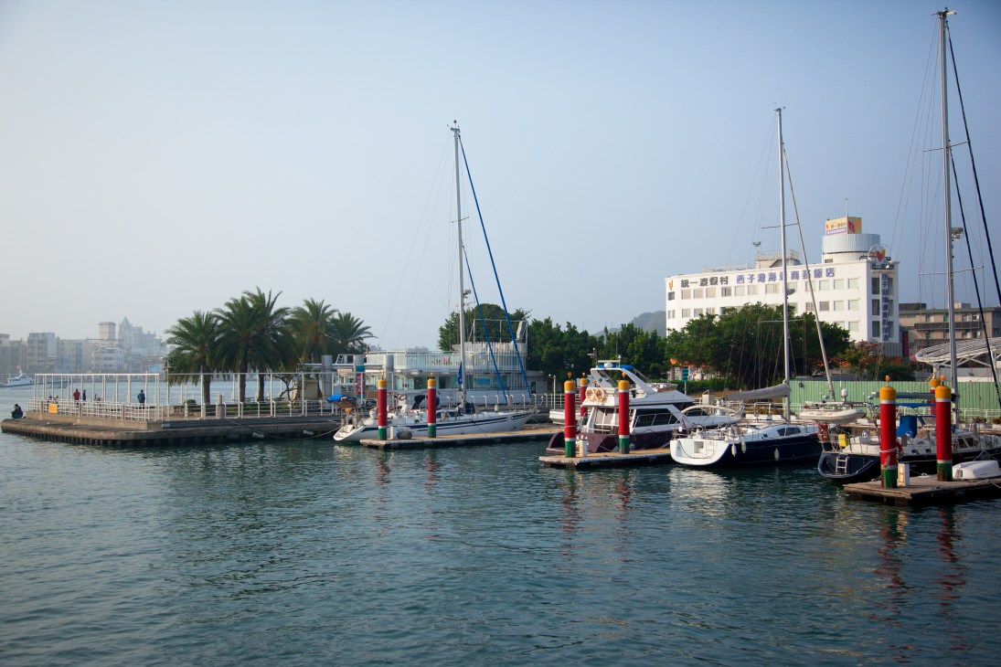 Sailboats and yachts docked at Gushan Ferry point with palm trees and waterfront buildings in the background.