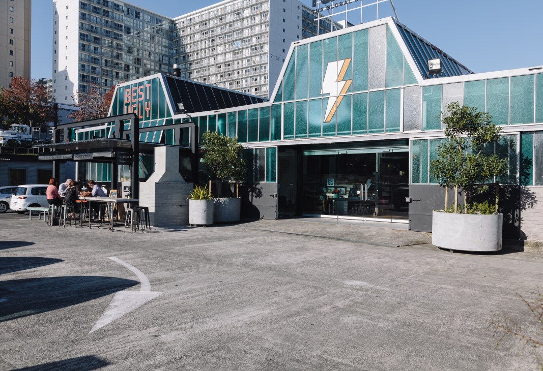 Exterior of the City Works Depot in Auckland showing a modern turquoise and white building with signage and people seated at outdoor tables.