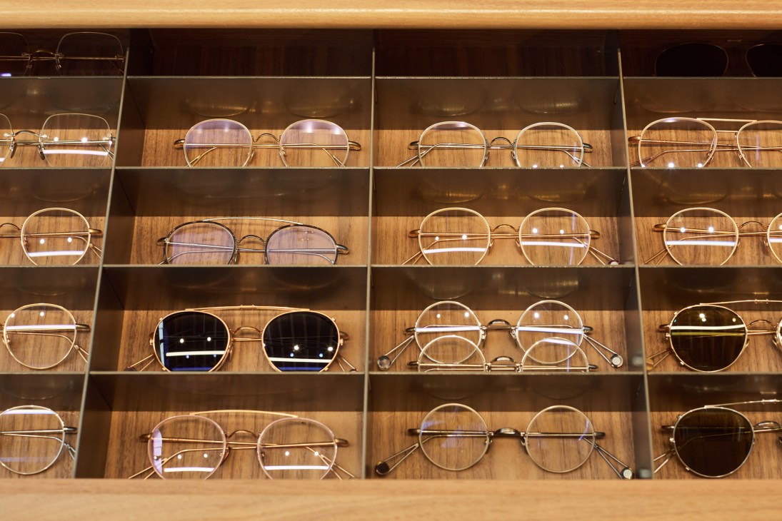 Display of Ahlem eyewear frames arranged on wooden shelves in a retail showcase, featuring round and geometric metal-framed designs.