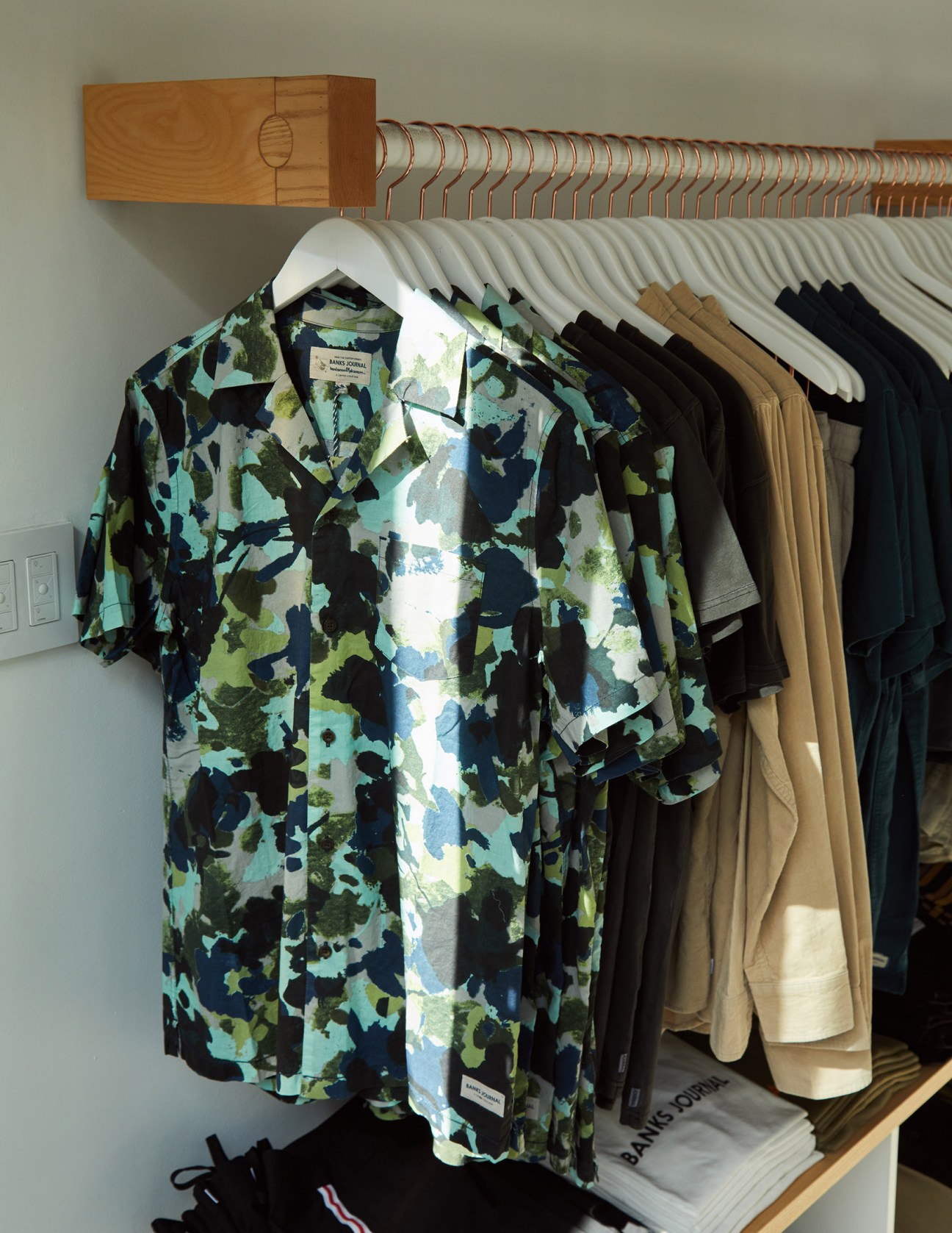 Colorful patterned shirts displayed on white hangers on a wooden rod at Banks Journal menswear shop.