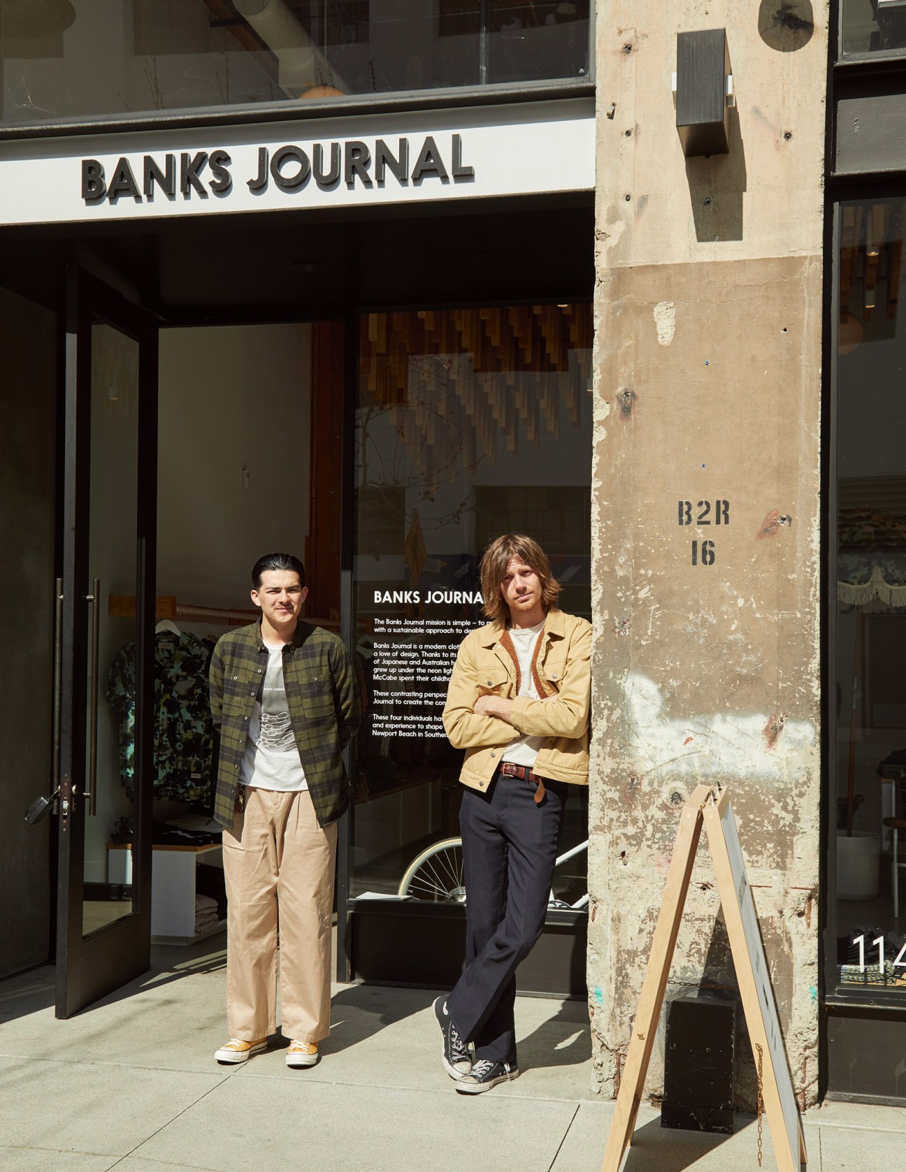 Two men stand outside the Banks Journal storefront on a sunny street in Downtown Los Angeles.