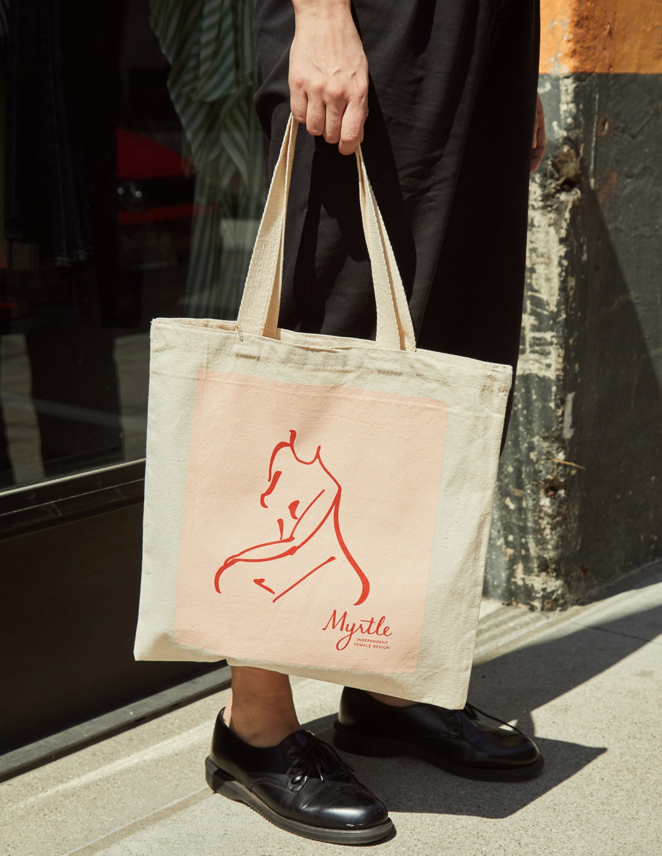 Person holding cream canvas tote bag with red line drawing of a horse and 'Myrtle' text.
