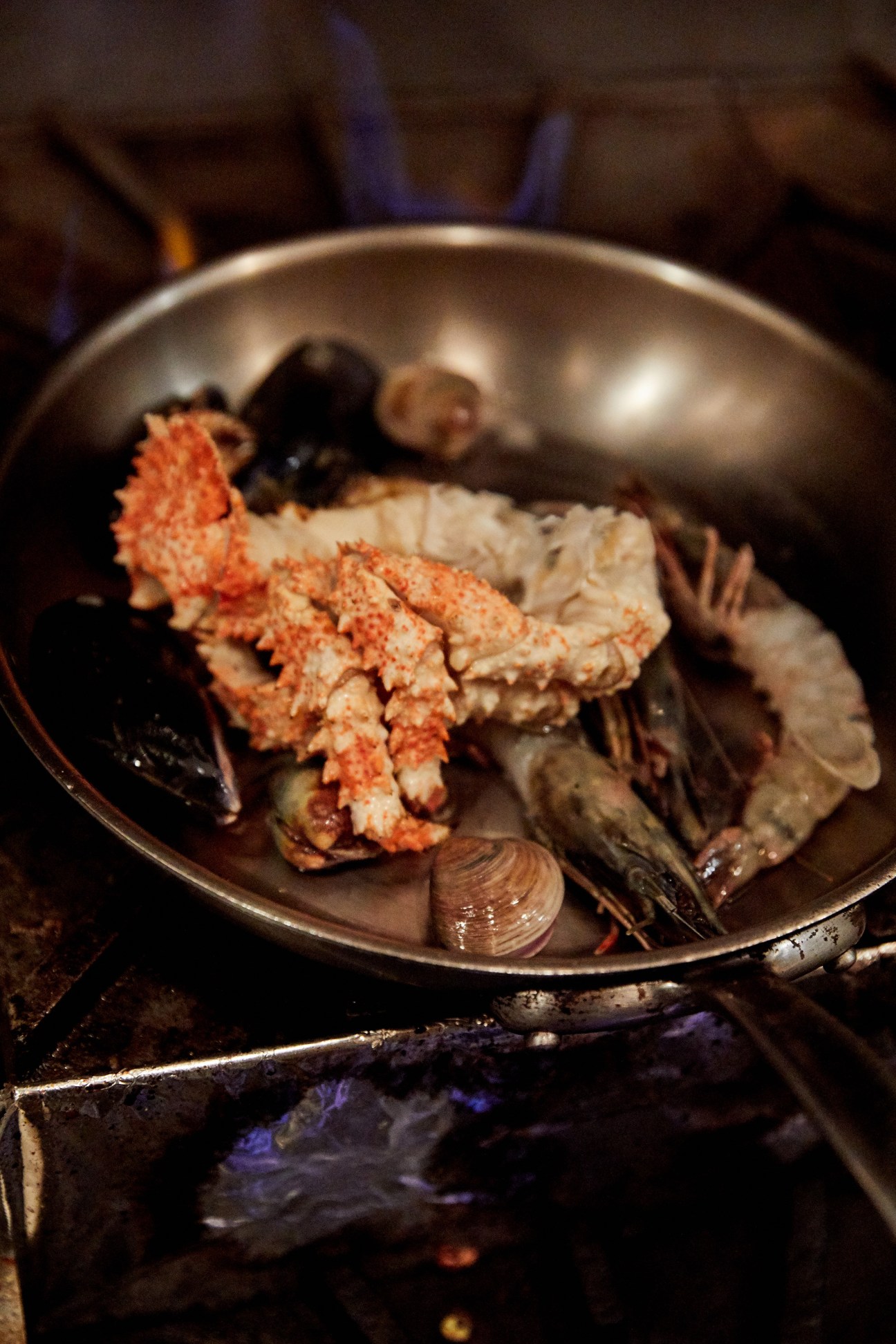 Fresh seafood including box crab, mussels, clams and shrimp cooking in a metal pan over blue flames