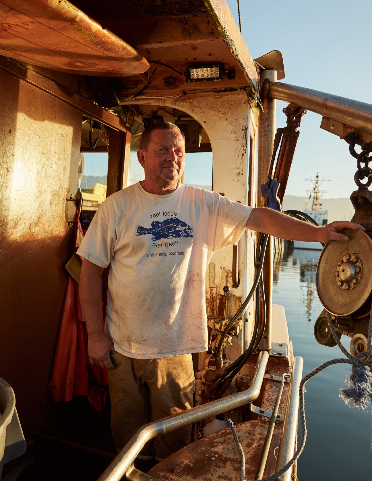 Fisherman Paul Teall in a white t-shirt standing on his fishing boat at Santa Barbara harbor