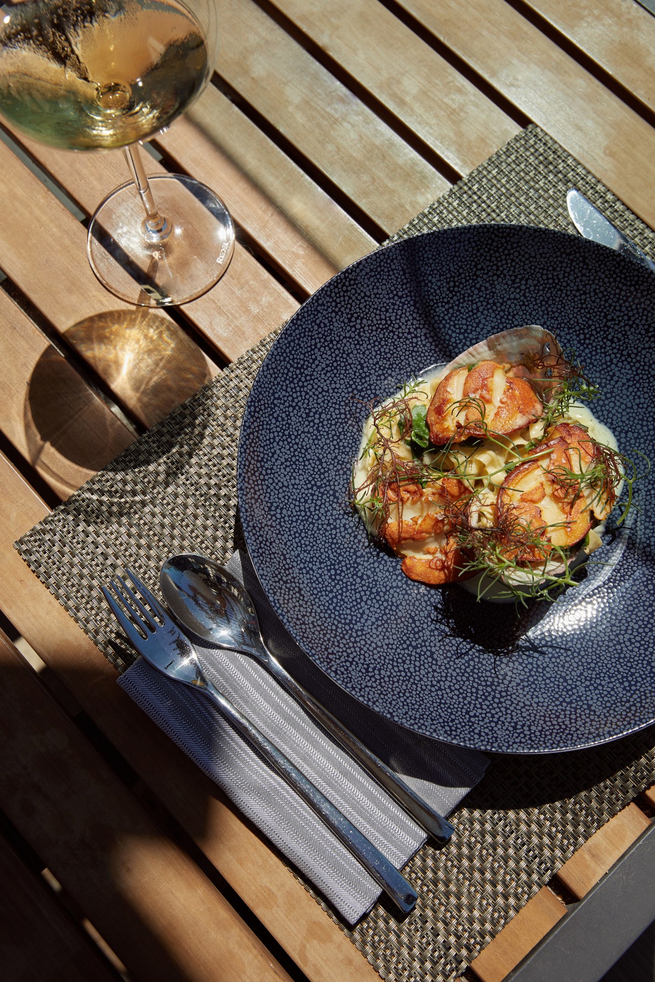 Seared scallops with creamy sauce and green garnishes on a textured dark blue plate at Ritz-Carlton