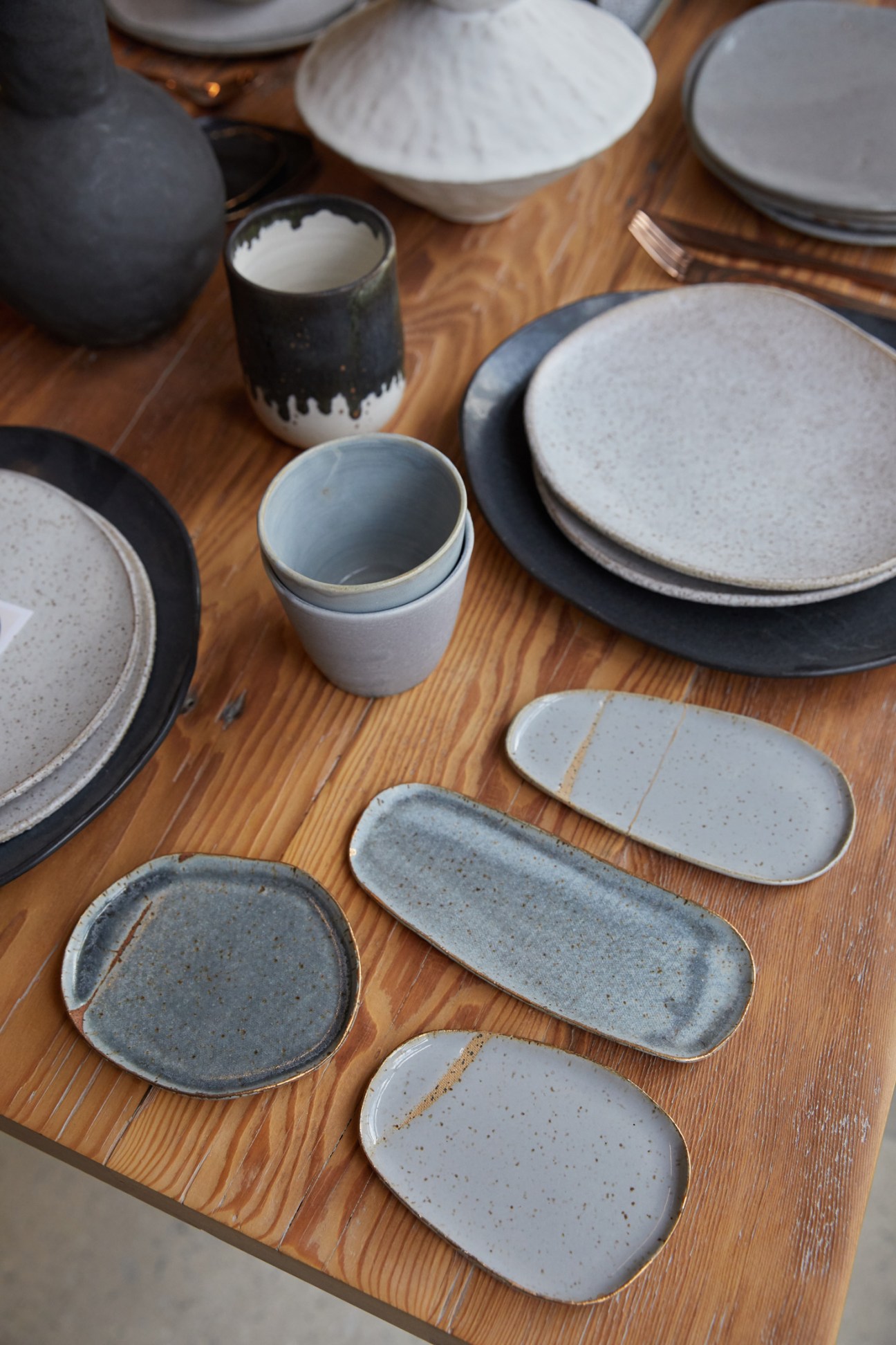 Assorted handcrafted ceramic plates, bowls and cups displayed on a wooden surface.