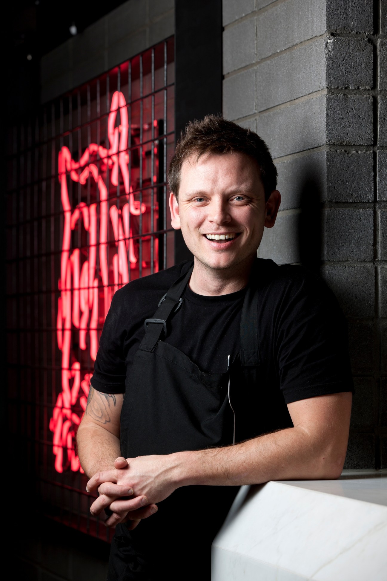 Chef Dylan Roberts smiling at Claremont Tonic bar with neon tiger sign behind him.