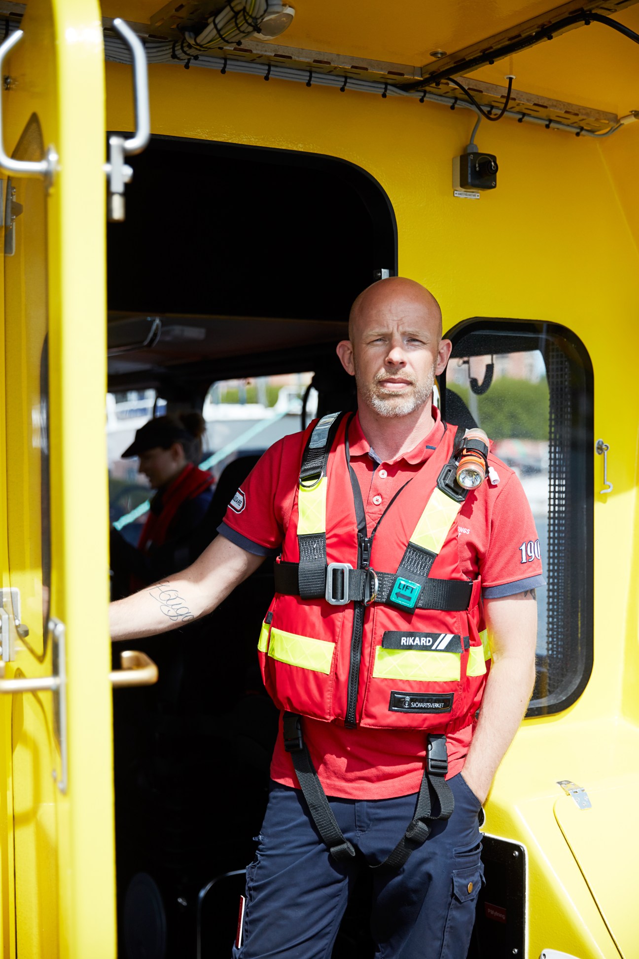 Swedish Sea Rescue Society volunteer in red and yellow safety gear standing in doorway of yellow rescue vessel.