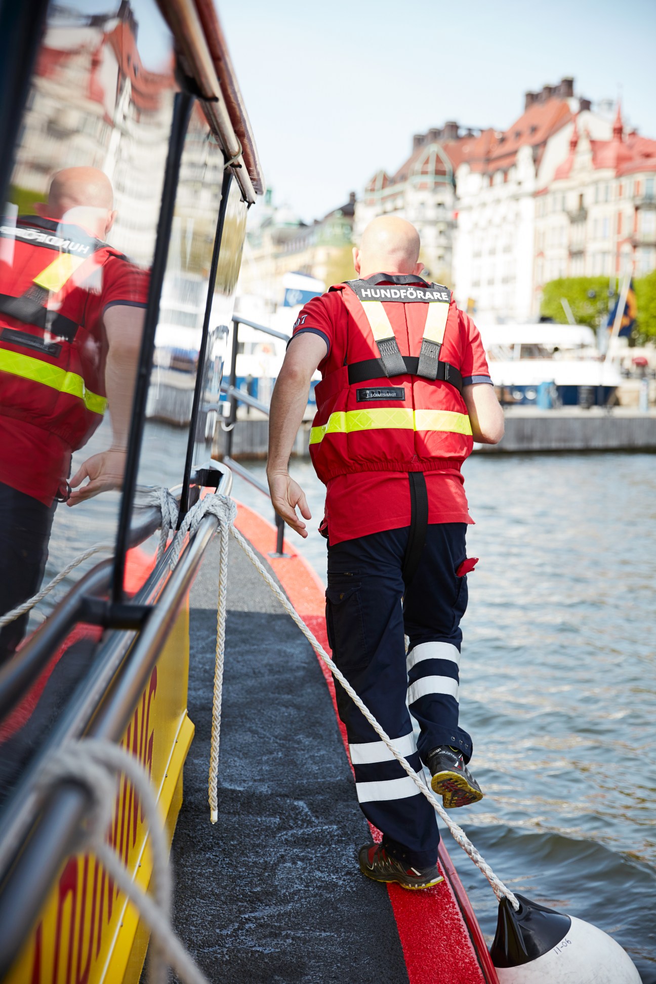 Swedish Sea Rescue Society volunteer in red lifejacket boarding rescue vessel in Stockholm harbor.