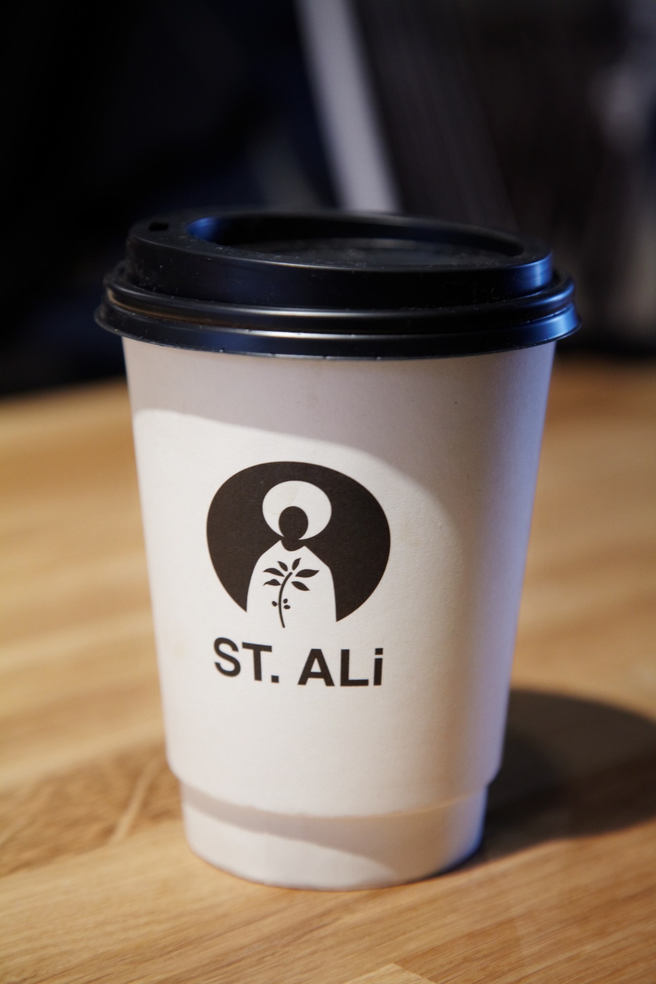 St Ali coffee cup with black lid on wooden surface showing the brand's logo