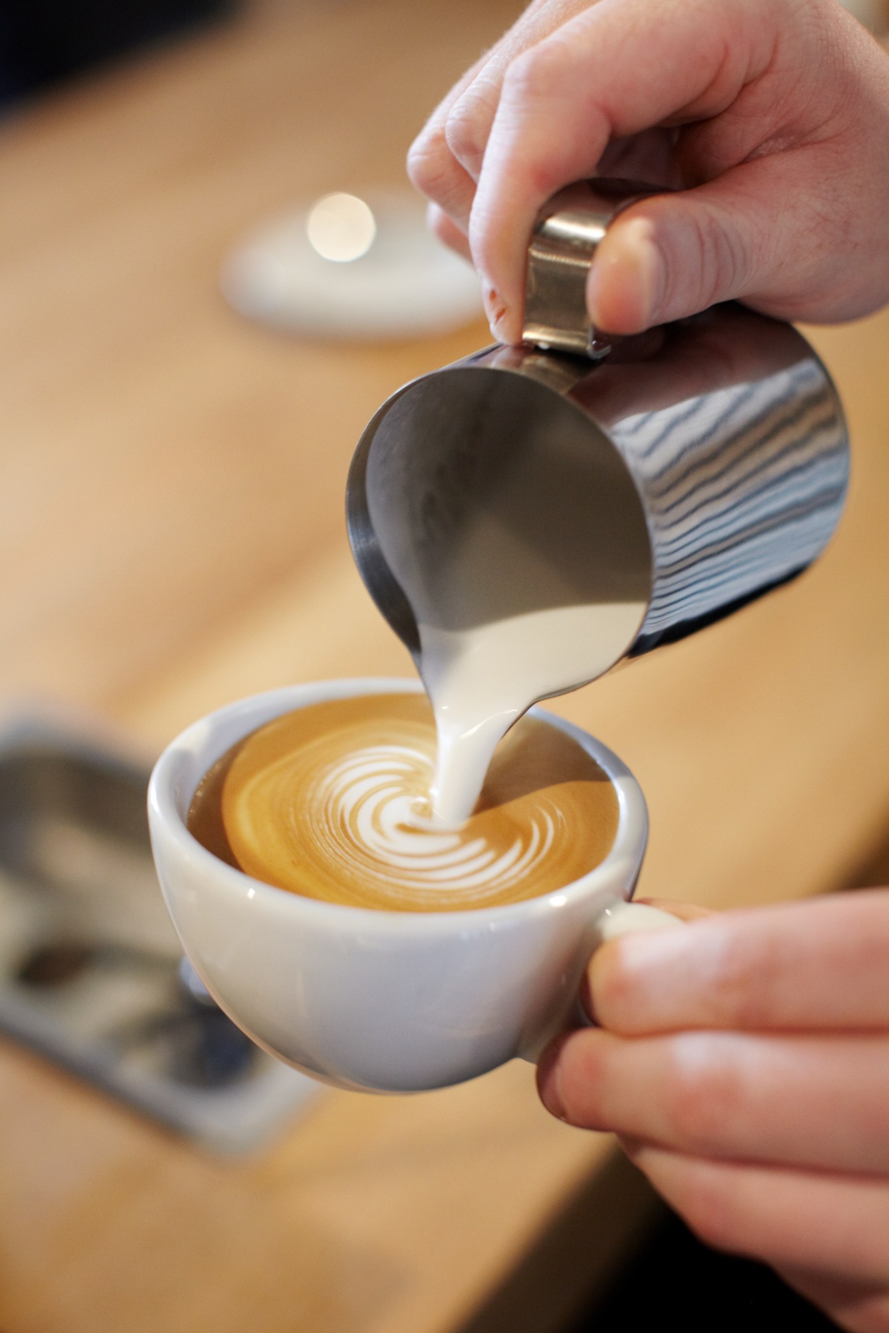 Barista pouring steamed milk into espresso to create latte art in white cup.