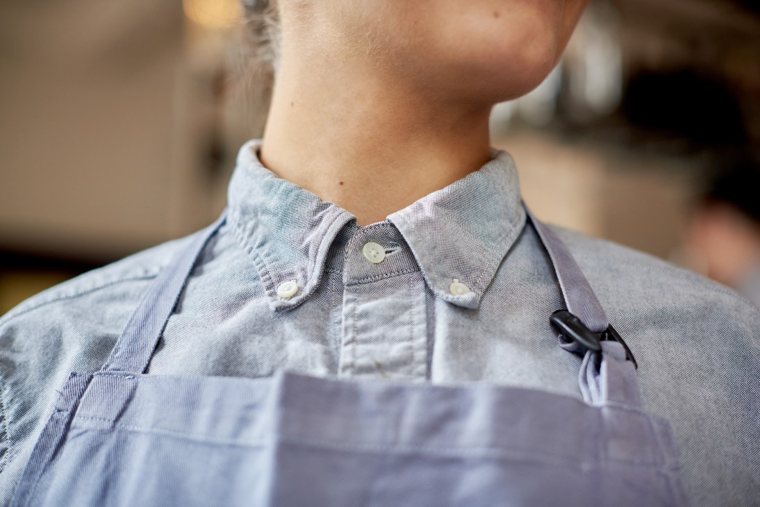 Close-up of a light grey Oxford shirt with button-down collar and grey apron, The Clove Club uniform.