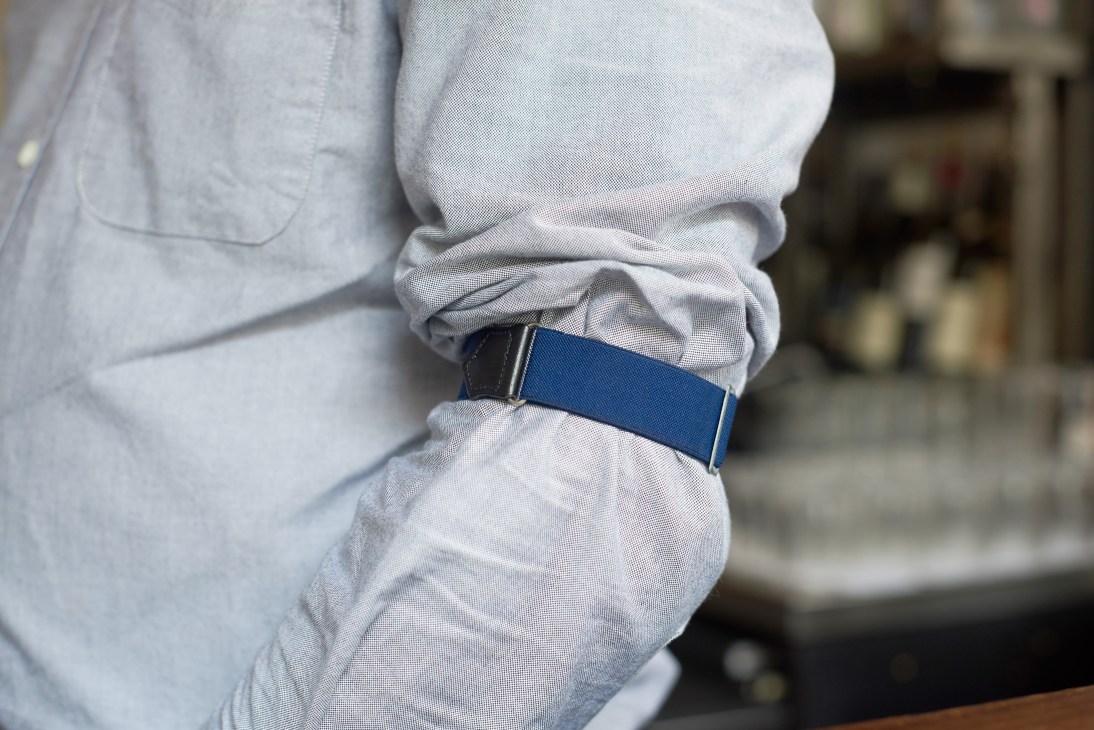 Close-up of light grey Oxford shirt sleeve with blue fabric belt detail from The Clove Club uniform.
