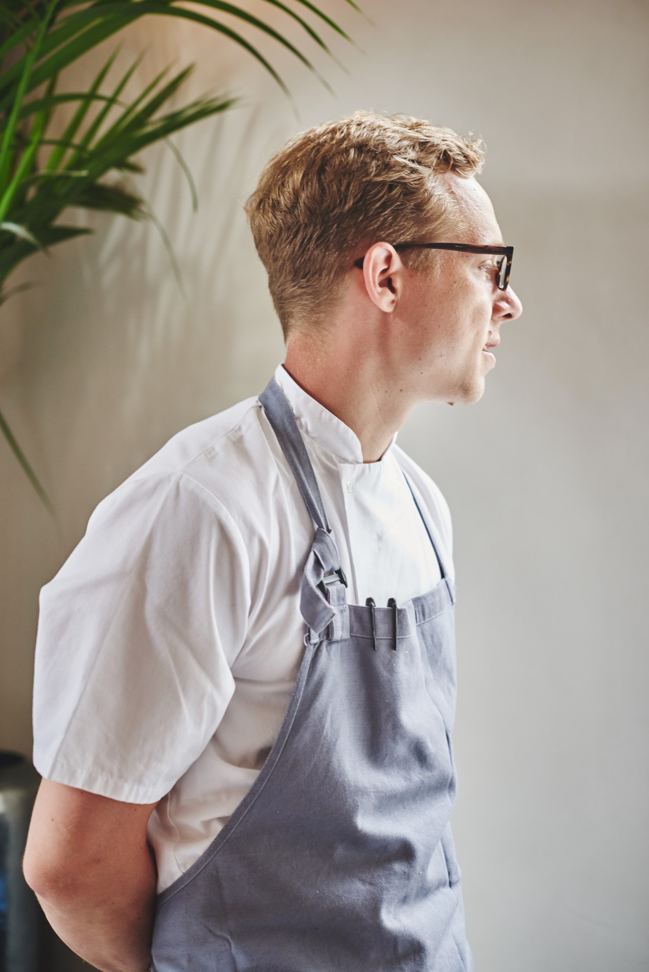 Man wearing light-grey Oxford shirt and grey apron uniform from The Clove Club restaurant.