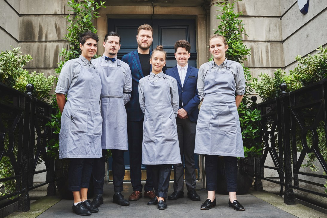 The Clove Club staff wearing light-grey Oxford shirts, chino-cut selvedge denim trousers and grey aprons outside restaurant entrance.
