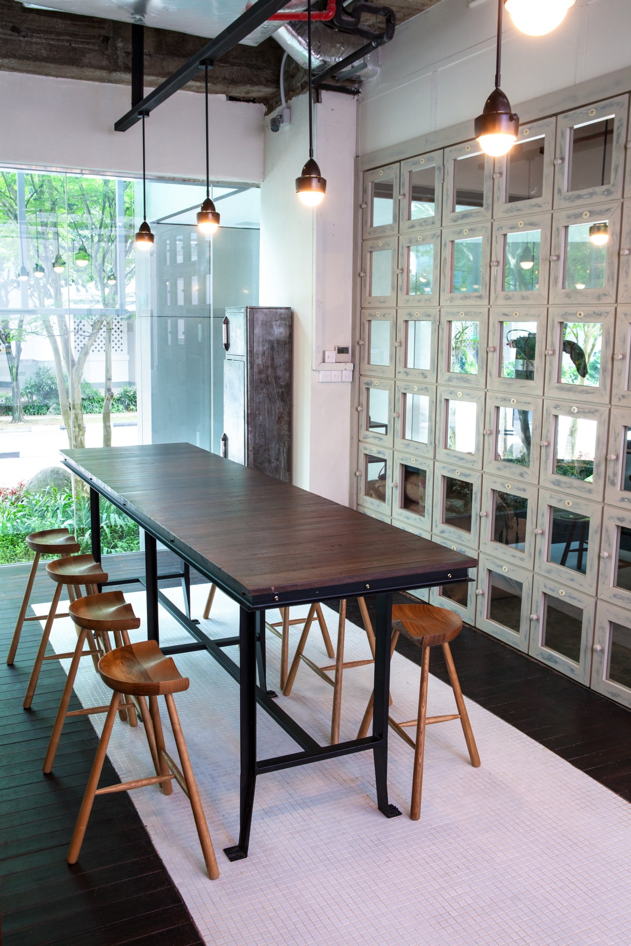 Interior of Common Man Coffee Roasters with long wooden table, wooden stools, pendant lights, and glass-fronted storage cabinets.