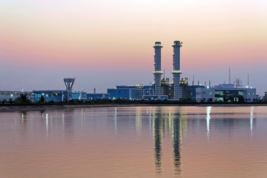 Industrial power plant with two tall smokestacks reflected in calm water at dusk.