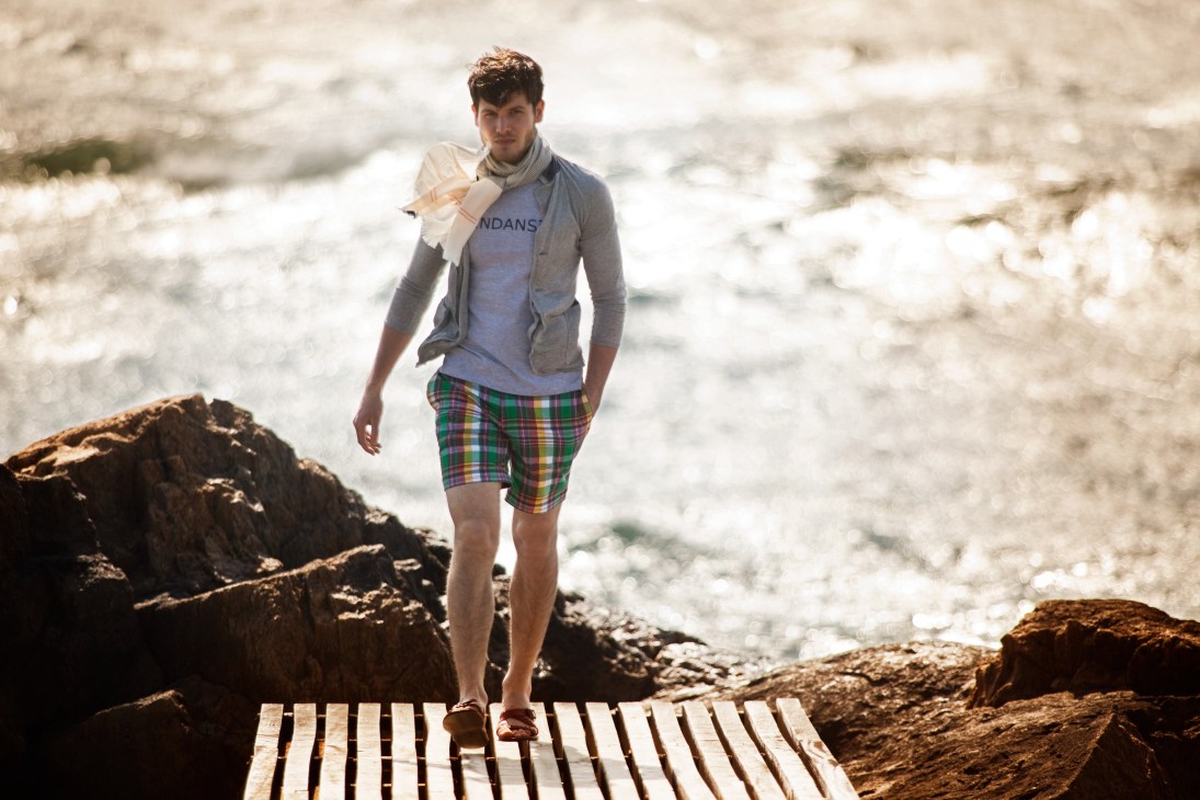 Man walking on wooden boardwalk along rocky Portuguese coast wearing casual beach attire.