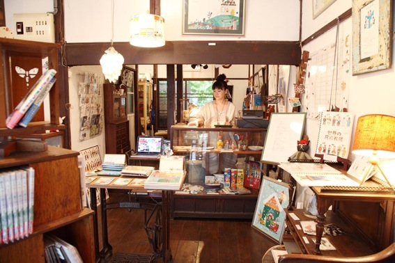 Interior of Colobockle shop in Tokyo showing wooden furniture, artwork, books, and handmade crafts displayed throughout.