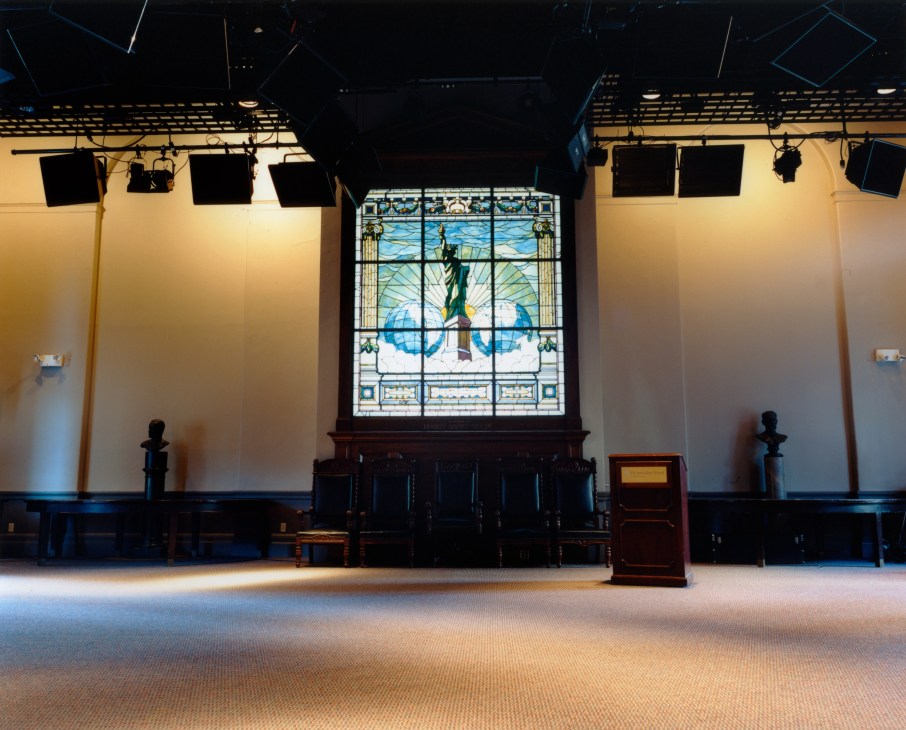Interior of Columbia University School of Journalism Student Center with stained glass window and stage lighting.