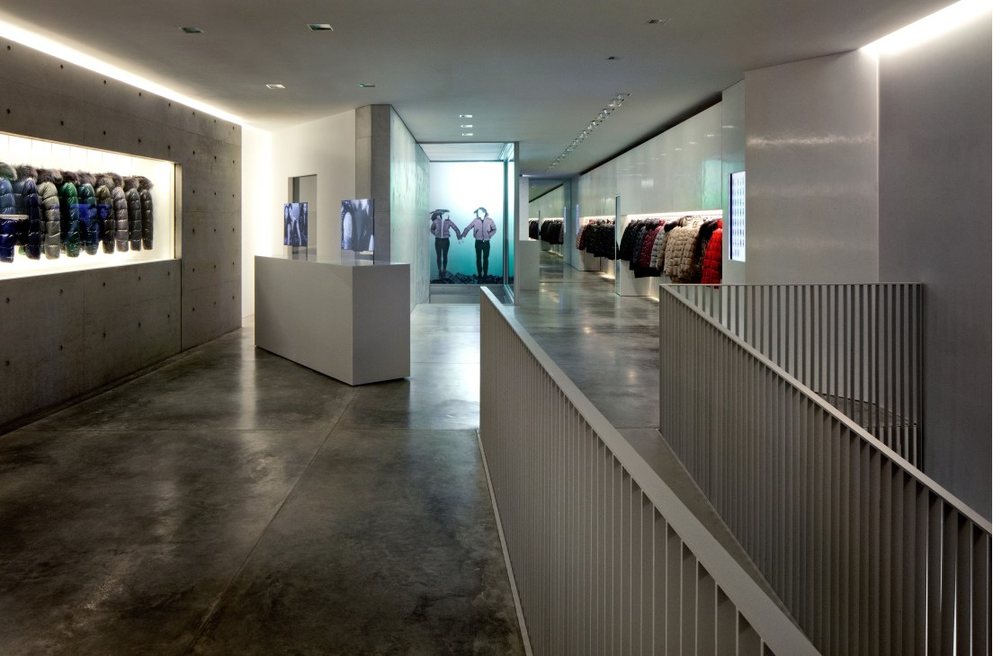Modern retail interior of Duvetica store in Milan with minimalist concrete walls, steel railings, and displayed down jackets.