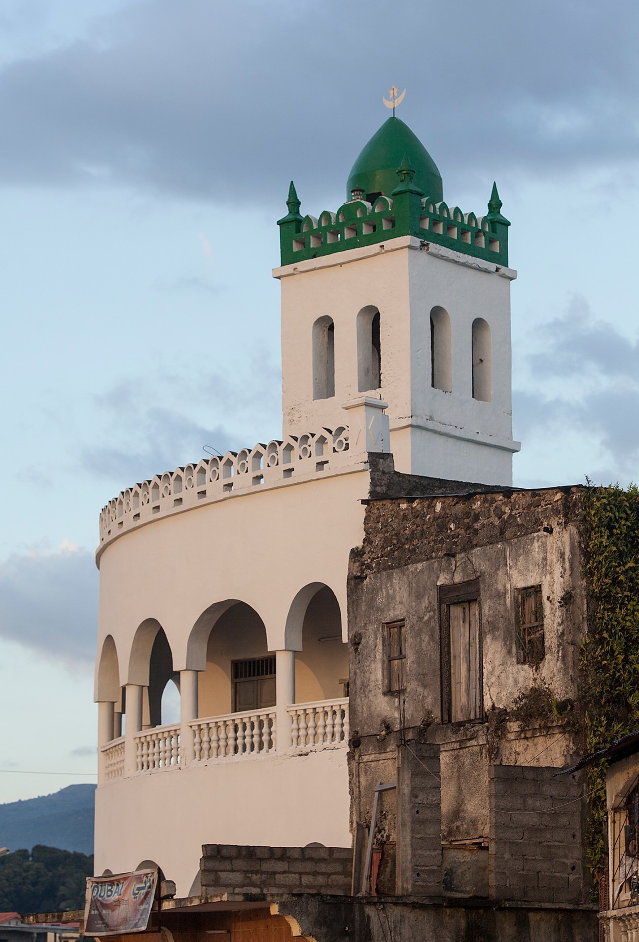 A half-restored mosque in Moroni with a green-domed minaret and cream-coloured walls, partially deteriorating structure.