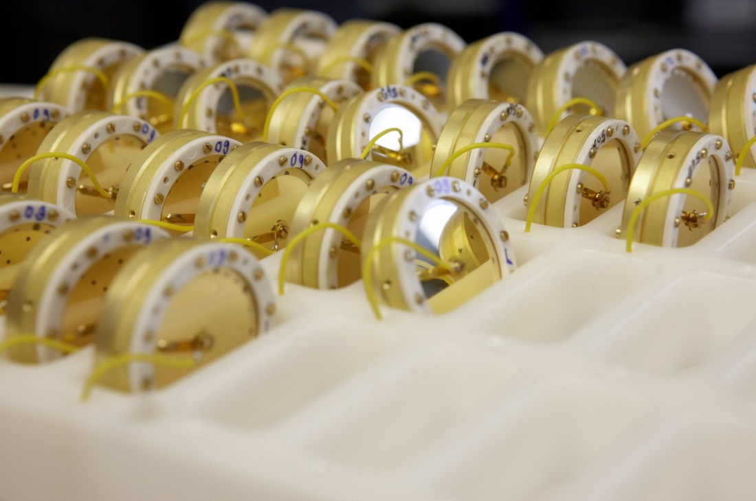 Multiple microphone condenser capsules with brass bodies and white ceramic sections arranged in rows.
