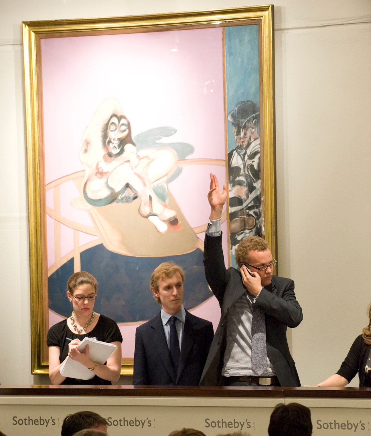 Sotheby's staff relay telephone bids in front of a Francis Bacon painting during an auction.
