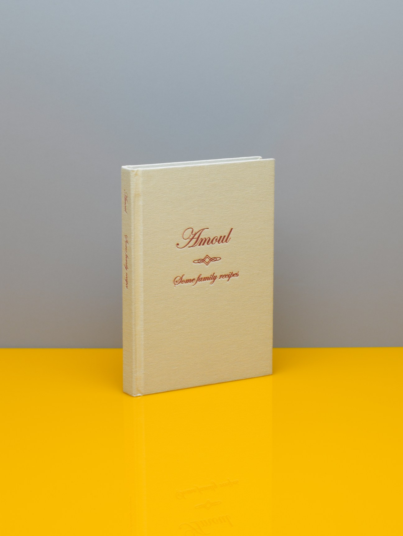 Cream-coloured hardcover cookbook titled 'Amoul Some family recipes' with red script lettering on grey and yellow background.
