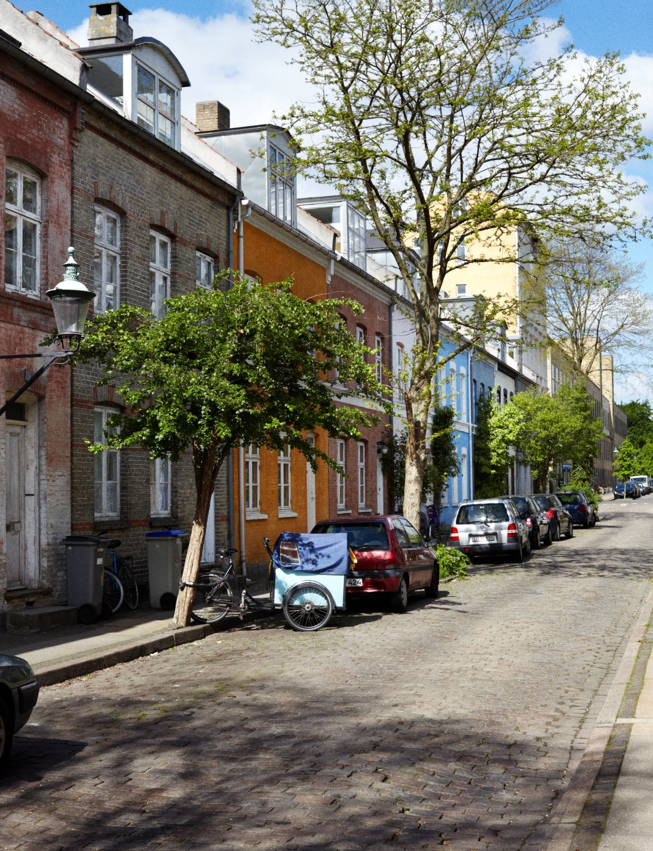 Colorful residential street in Copenhagen with parked bicycles, cars, and leafy trees along brick buildings.