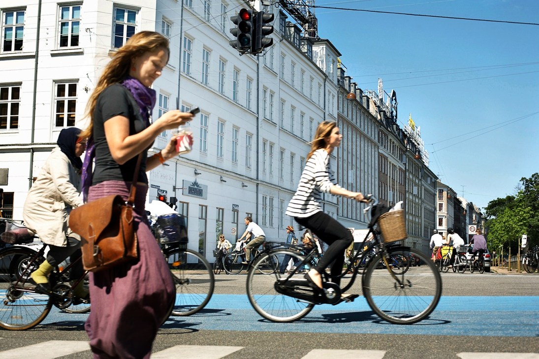 Cyclists riding on a blue-painted bike lane in Copenhagen with historic European buildings in the background.