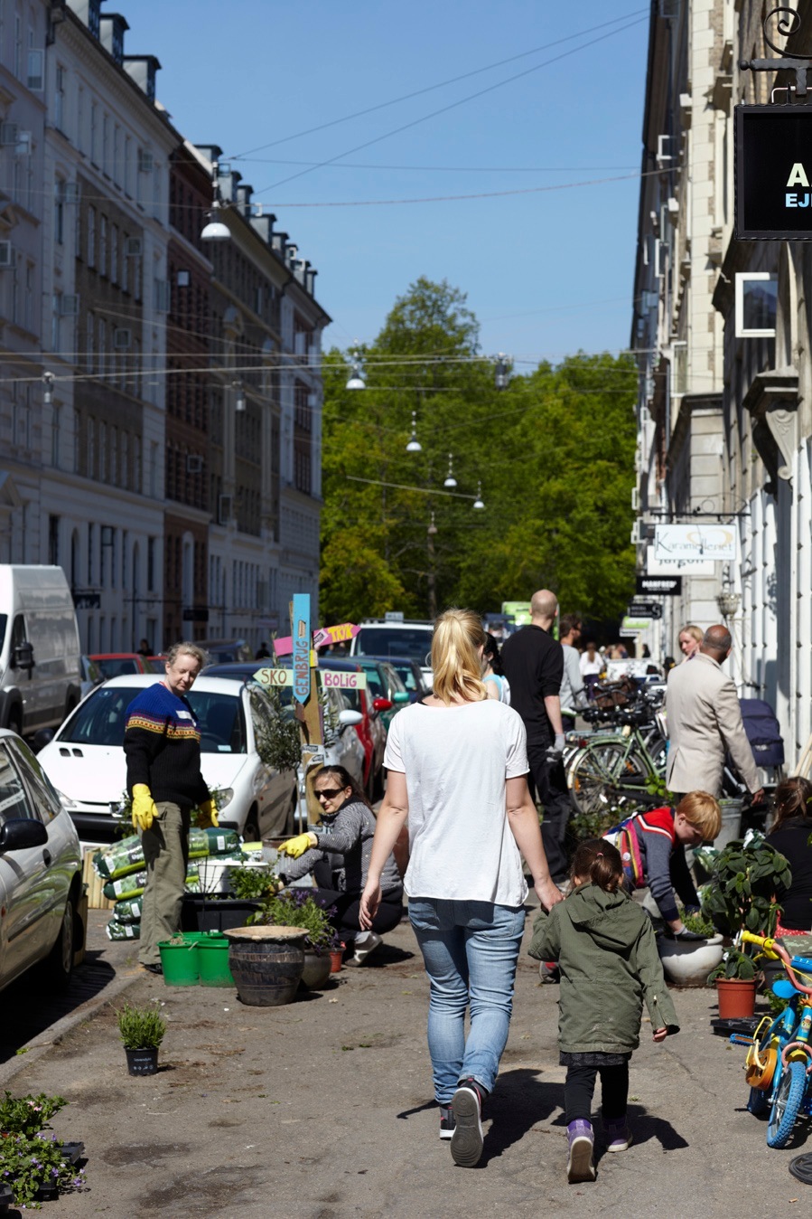Street market scene in Copenhagen with woman and child walking among vendors and plants.