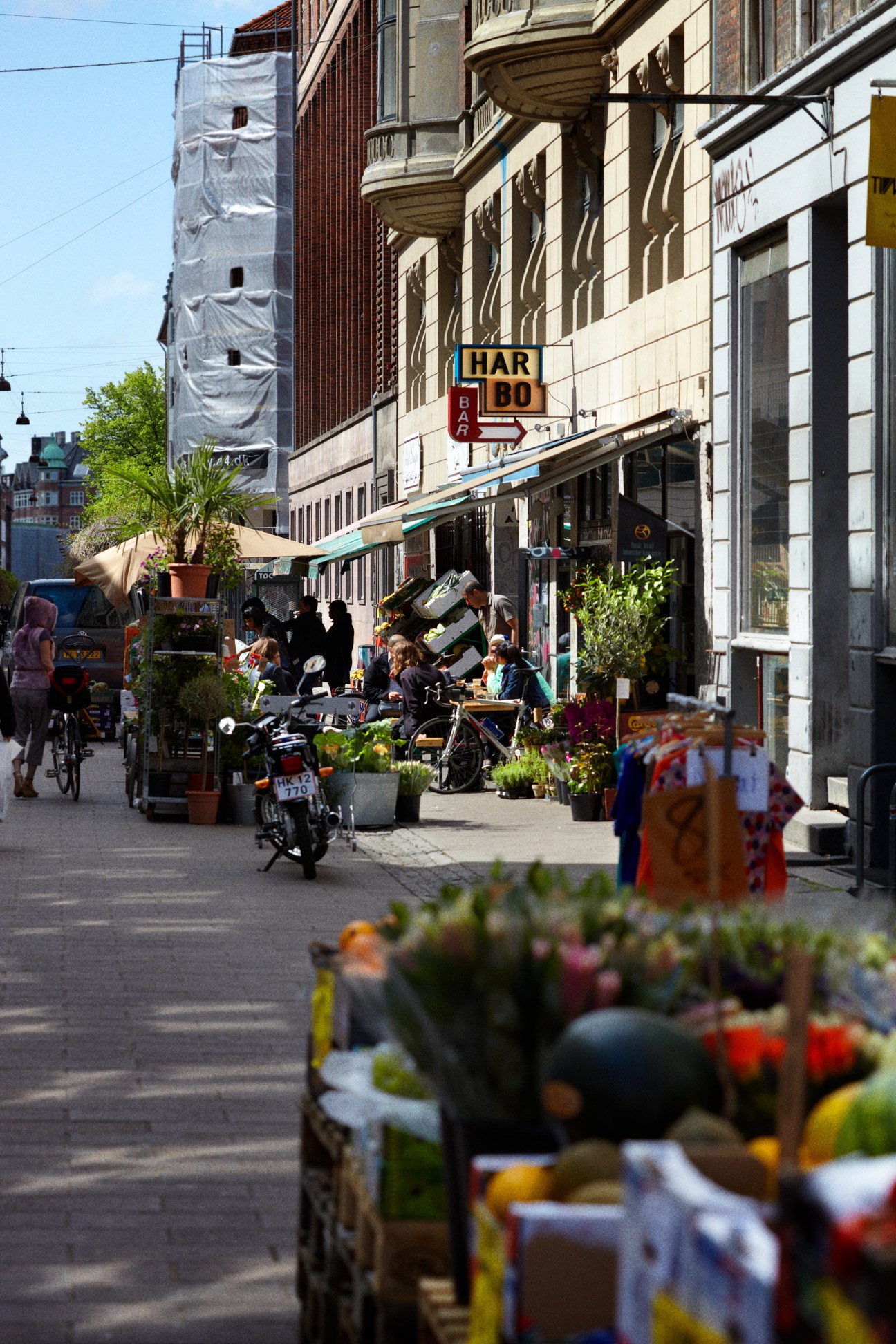 Copenhagen street scene with cyclists, outdoor café seating, potted plants, and historic buildings.
