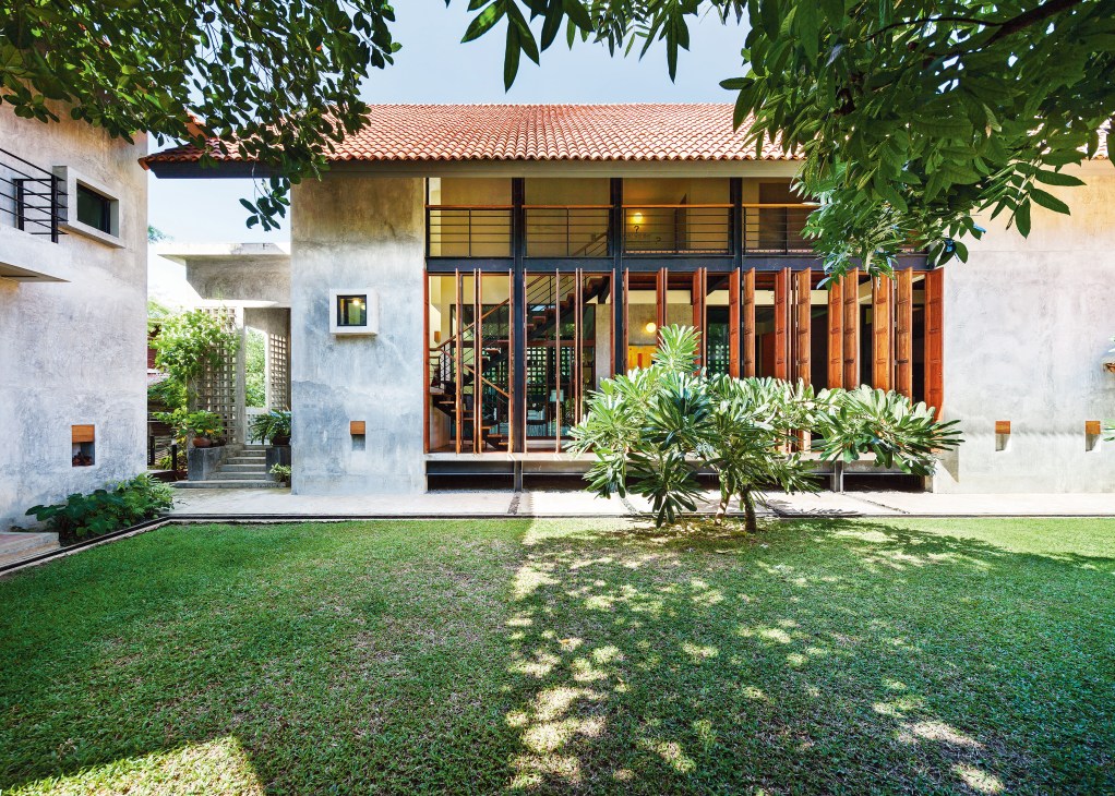 Modern concrete house with red clay tile roof, wooden folding doors, and tropical landscaping in garden courtyard