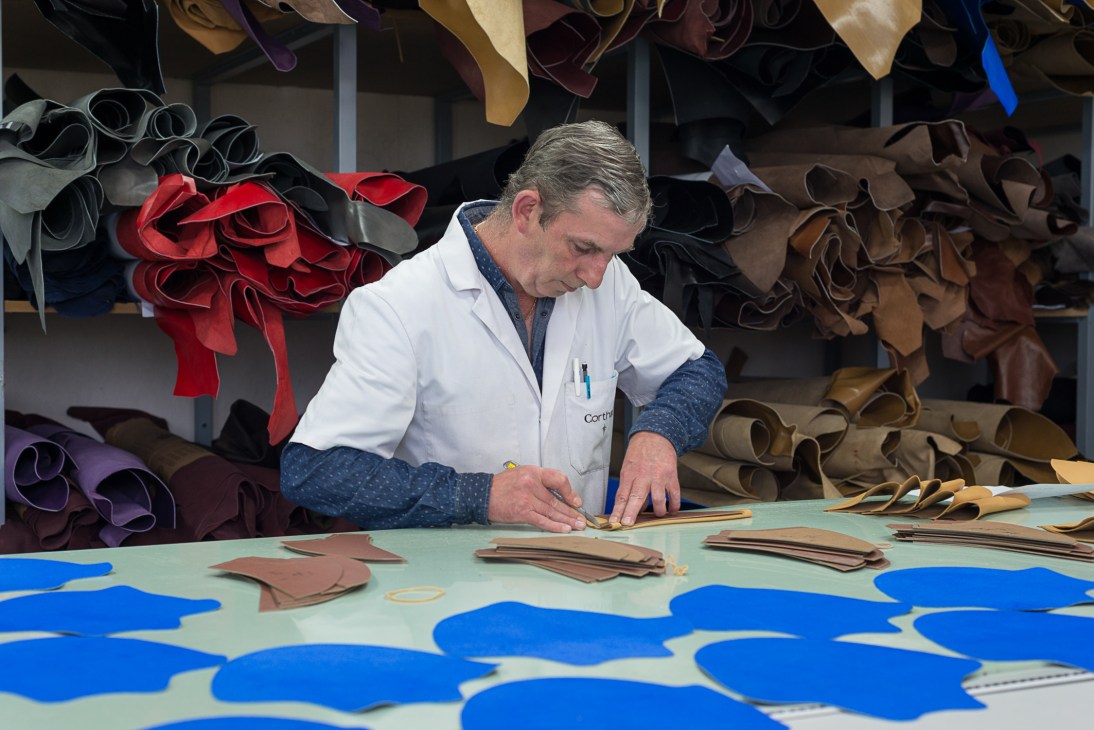 Craftsman at Maison Corthay cutting leather patterns for shoe uppers at a work table.