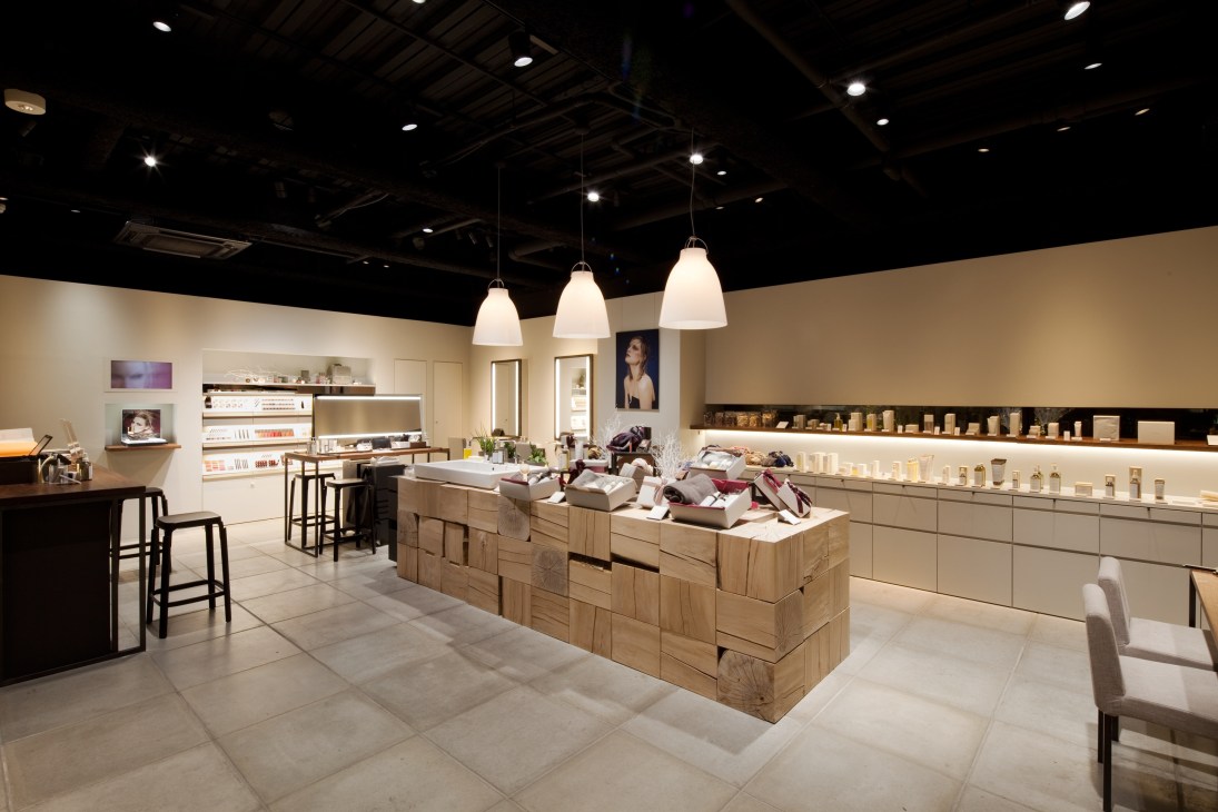 Interior of Three's minimalist cosmetics salon with raw wood display tables and pendant lights.