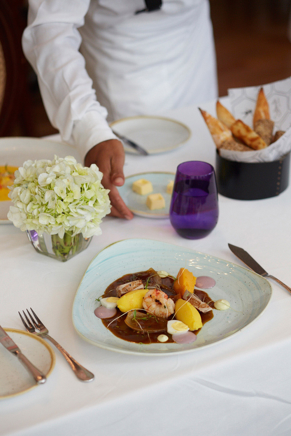 A plated causa escabechada dish with shrimp, potatoes, and garnishes at an upscale restaurant table.