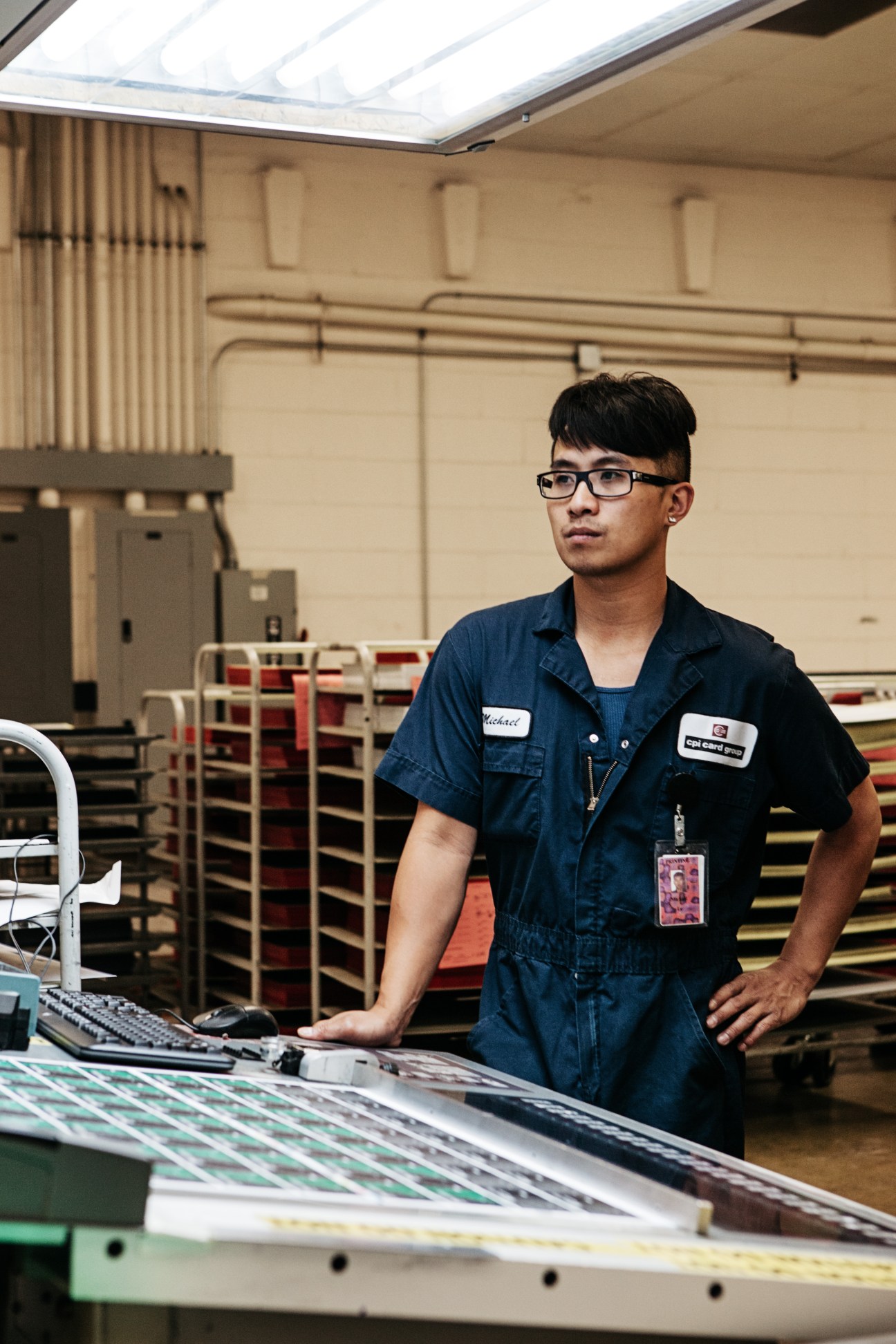 Male worker in blue uniform and glasses standing at workstation in CPI manufacturing facility.