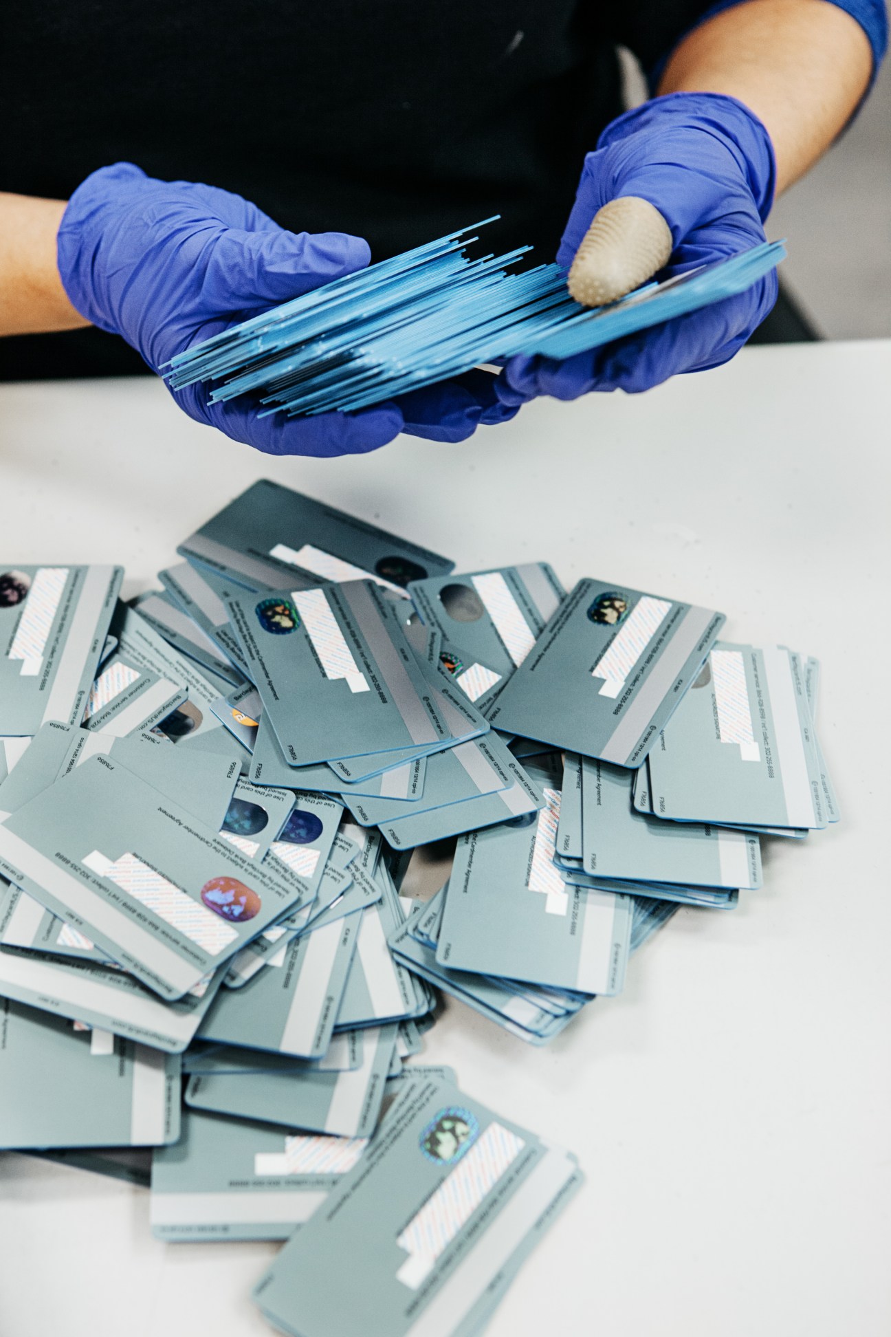 Hands in blue gloves holding stacks of blue plastic bank cards with embedded chips.