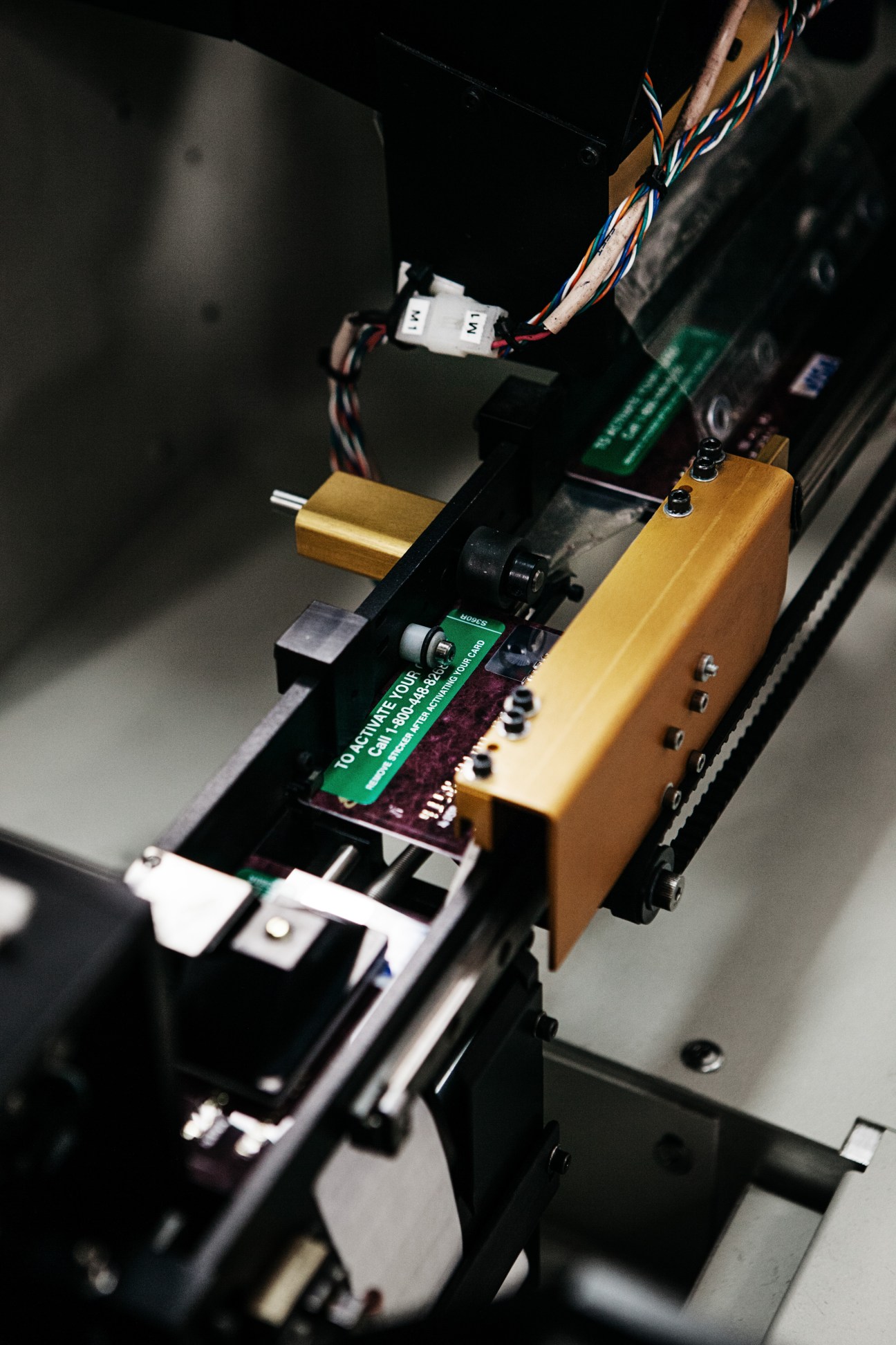 Close-up of electronic equipment showing circuit boards, wiring, and gold-colored components during card personalization process.