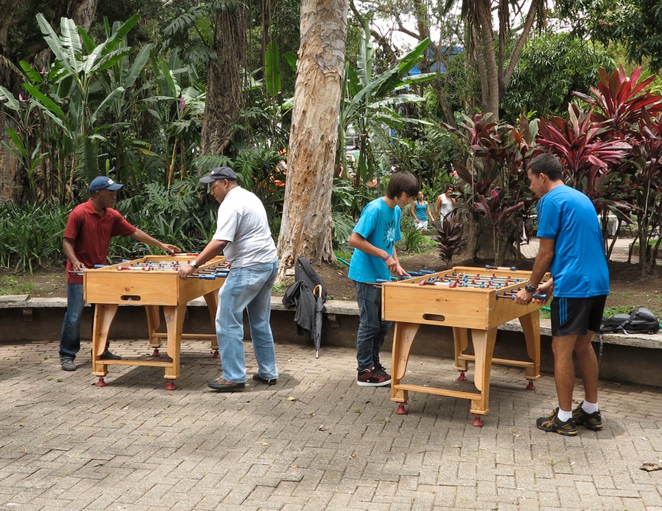People playing table football in a park surrounded by tropical plants and tall trees in San José.