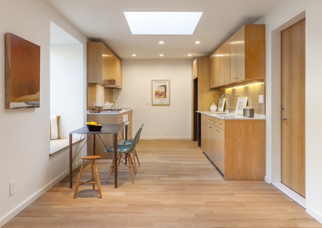 Open-plan kitchen and dining area with white-oak cabinets, skylights, and minimal furnishings in a compact home.
