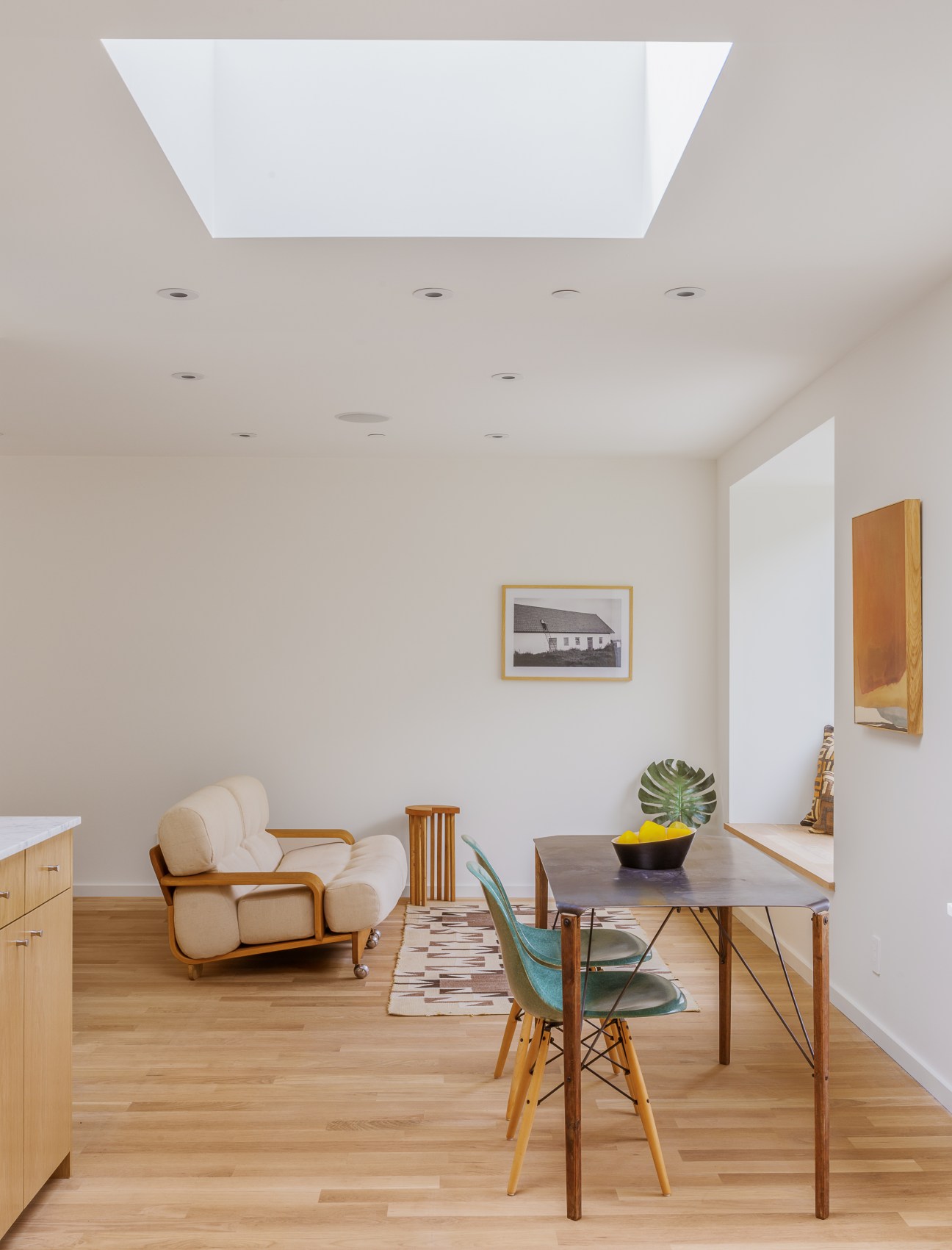 Interior living space with white oak flooring, skylights, mid-century furniture, and minimal white walls in a compact home.