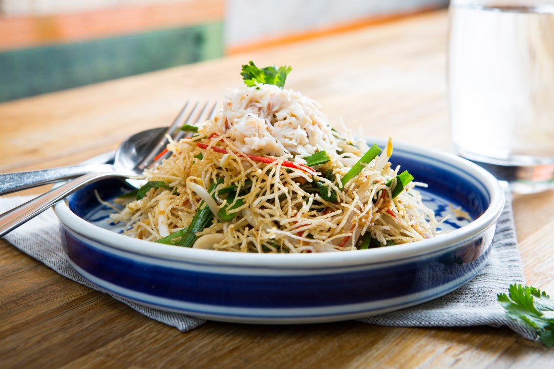 Crispy noodles with crab and fresh herbs served on a blue-rimmed white plate at The Begging Bowl, Peckham.