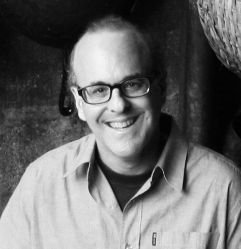 Mark Brownstein, a man wearing glasses and a light-colored shirt, smiling at the camera in black and white.