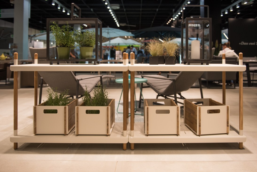 Cane-line's Frame shelves display with wooden structure, white shelving, potted plants and wooden storage boxes at a garden trade fair.