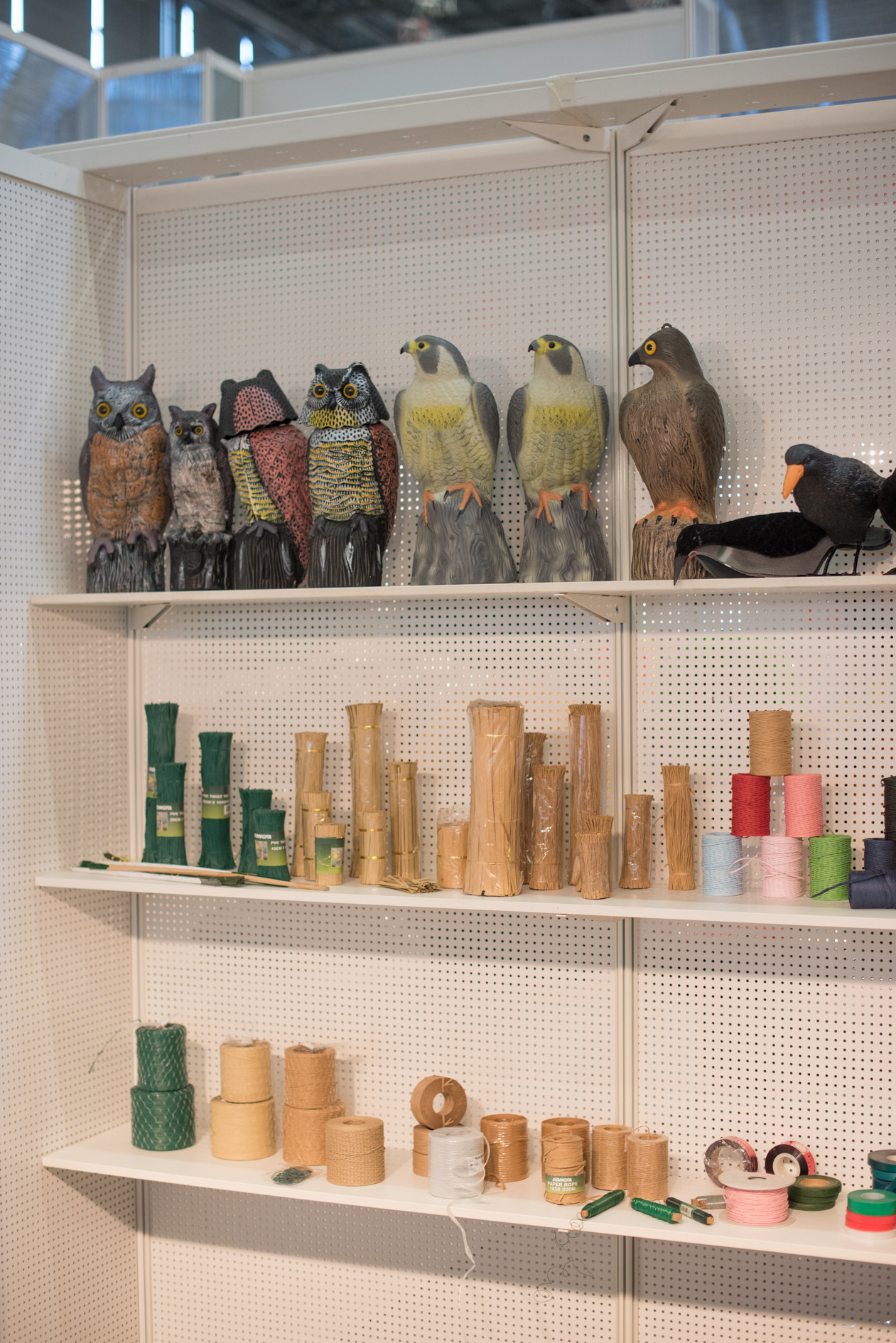 Plastic decorative bird figurines displayed on shelves alongside craft supplies and spools of thread at a trade fair booth.